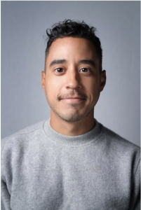 Drew Arrieta pictured wearing a gray sweater, looking at the camera.